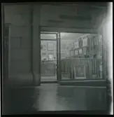 1950. Paris. En man sittter inne i en butik med konst, kväll