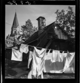 539 Söder. Tvätt hänger på tork framför en träkåk i Vitabergsparken. Sofia kyrka i bakgrunden.