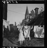539 Söder. En kvinna hänger tvätt framför en av träkåkarna i Vitabergsparken.