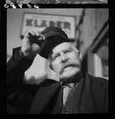 539 Söder. Porträtt av en man i mustasch som lyfter på kepsen.