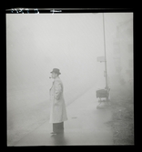 542 Dimma. En man som röker pipa väntar i dimman vid en hållsplats.