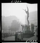 542 Dimma. Människor vid fontänskulpturen Orfeusgruppen av Carl Milles framför Konserthuset på Hötorget i Stockholm.