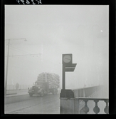 542/B Dimma. En lastbil med flaket fullt av säckar passerar på en bro. En klocka i förgrunden.