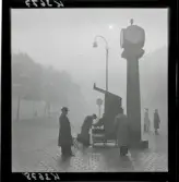 542/B Dimma. Män väntar på ett torg. Skoputsare i arbete intill en klockstapel.