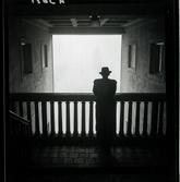 542/B Dimma. En man i hatt står vid ett räcke och tittar ut i dimman.