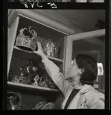 561 Operan för Allers. Kostymförråd. En kvinnlig arbetare sträcker sig efter en huvudkrona i ett skåp.