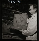 561 Operan för Allers. Kostymförråd. En man arbetar bland stövlar och skor, håller fram en enorm stövel.