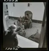 568 F. Stieg Trenter, Torremolinos. Begravning. Sörjande har samlats vid kistan framför kyrkan.En kvinna betraktar dem från ett fönster.