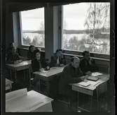 584 Brunsviks Folkhögskola. Studenter sitter i sina skolbänkar invid stora fönster i ett klassrum.