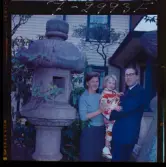 585/8 Facit Tokyo Daberg. En familj står i en trädgård vid en japansk lykta av sten. Barnet är klädd i kimono.