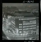 585/40 Facit Nattbild från N.K + Södra Kungstornet. Kvällsbild. Facit-skylt på taket av fastigheten Styrpinnen 22, ritad av arkitekt Ivar Tengbom i hörnet Hamngatan / Kungsträdgårdsgatan i Stockholm.