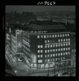 585/40 Facit Nattbild från N.K + Södra Kungstornet. Kvällsbild. Facit-skylt på taket av fastigheten Styrpinnen 22, ritad av arkitekt Ivar Tengbom i hörnet Hamngatan / Kungsträdgårdsgatan i Stockholm.