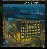 585/40 Facit Nattbild från N.K + Södra Kungstornet. Kvällsbild. Facit-skylt på taket av fastigheten Styrpinnen 22, ritad av arkitekt Ivar Tengbom i hörnet Hamngatan / Kungsträdgårdsgatan i Stockholm.
