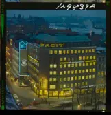 585/40 Facit Nattbild från N.K + Södra Kungstornet. Kvällsbild. Facit-skylt på taket av fastigheten Styrpinnen 22, ritad av arkitekt Ivar Tengbom i hörnet Hamngatan / Kungsträdgårdsgatan i Stockholm.