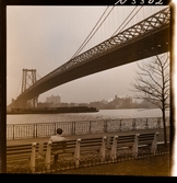1690 New York allmänt (N.Y. Herald Tribune). George Washington bridge. En man sitter på en bänk under bron.