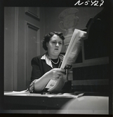 1690 New York allmänt (N.Y. Herald Tribune). En kvinna sitter vid en kassapparat och läser tidningen.