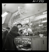 1690 New York allmänt (N.Y. Herald Tribune). K W Gullers blir visad en kamera av en expedit i butik.