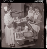 1711 En sjuksköterskas arbetsdag. Mat portioneras ut från en vagn.