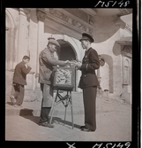 1717/K Istanbul allmänt. Gatuförsäljare. En man säljer bröd till en turistande man i uniform.
