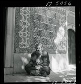 1717/K Istanbul allmänt. En man sitter på trottoaren framför en fasad med mönstrat kakel.