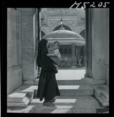 1717/K Istanbul allmänt. En kvinna med ett litet barn i famnen står i ingången till gården vid moské.