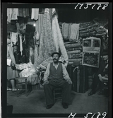 1717/K Istanbul allmänt. En man sitter framför en butik  som säljer mattor, eventuellt marknaden i Grand Bazaar.