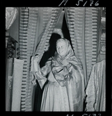 1717/K Istanbul allmänt. En kvinna håller en schal kring huvudet, står under ett draperi i en dörröppning.