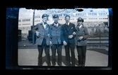 Porträtt av fyra män, tre i arbetsuniformer, ståendes på perrong, tågstation.
