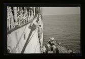 En man klättrar i en repstege från ett fartyg till en båt nedanför.