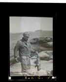 En man står på en klippa vid havet med sin fångst, en liten säl.