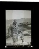 En man står på en klippa vid havet med sin fångst, en liten säl.