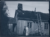 Två unga kvinnor framför ett hus. En stege står uppställd mot taket.