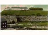 Kolorerat vykort. Utsikt mot fästningen med vallgraven i förgrunden. T v uppe på fästningsvallen står den sista kanonen på fästningen. Den flyttades till Påskberget 1898.
(Bild 2: motivet i sv/v)