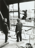 Nya Teaterhuset byggs upp 1997 - 1998. En person står utomhus på en byggnadsställning. Inne i lokalen står två män och ser på.