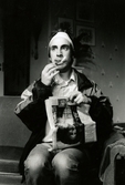 Nya Teaterhuset okänt årtal. Skådespelaren och komikern Per Andersson vid en repetition eller föreställning. Han sitter på en stol och har något på huvudet samt en cigarett i munnen. I knäet har han en tidning.