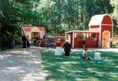 Förberedelser inför sommarspel/barnteaterföreställning, troligtvis 1999. Vid Byxorna i Gunneboskogen (korsningen Christina Halls väg/John Halls väg). Några personer står och tittar på slutresultatet av scenen, publikstolar och kiosken till höger. På gräsmattan sitter några och fikar.
