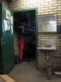 Verkstadsmiljö. En dörröppning till ett annat utrymme. Till höger om dörröppningen ett handfat samt en spegel. Interiörfotografi från byggnad vid Soabs industrianläggning i Mölndals Kvarnby, år 2007. Anläggningen användes vid fototillfället av Hexion Speciality Chemicals Sweden AB.