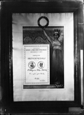 Fotografi av diplom: Almänna konst- och industri utställningen. Stockholm 1897. Diplom för silvermedalj.
En barbröstad kvinna till höger om diplombilden håller en lagerkrans i höger hand och lyfter den snett uppåt.