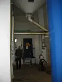 Utrymme med ett utlopp i taket. En man står intill en blå metalldörr med skyltar som varnar för gift. Interiörfotografi från byggnad vid Soabs industrianläggning i Mölndals Kvarnby, år 2007. Anläggningen användes vid fototillfället av Hexion Speciality Chemicals Sweden AB.