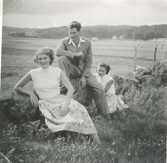 Tre ungdomar poserar sittandes på en gärdesgård, Backen eller Högen okänt årtal. I bakgrunden ses åkrar. 1. Okänd kvinna. 2. Lennart Pettersson. 3. Okänd kvinna.