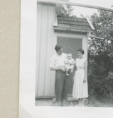 Karl Gustaf Pettersson och hustrun Dagny poserar framför en ytterdörr. I famnen håller Karl Gustaf sonen Lennart (född 1958), Backen eller Högen (övre gården) 1959.