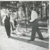 Fyra vuxna personer befinner sig på gårdsplanen vid Backen eller Högen 1960-tal. Från vänster: 1. Okänd äldre man med käpp. 2. Ester Pettersson (med förkläde, 1894 - 1988). 3. Okänd sittande kvinna. 4. Gående man.