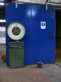 En grön våg och en blåmålad branddörr i en lagerlokal. Interiörfotografi från Soabs industrianläggning i Mölndals Kvarnby, år 2007. Anläggningen användes vid fototillfället av Hexion Speciality Chemicals Sweden AB.