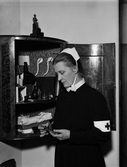 Utställningen Den gamla goda tiden - syster Elisabet Dillner framför sitt unika medicinskåp, Uppsala 1942