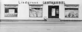 Närbild av entrén till Lindgrens lanthandel på Gamla Riksvägen 42 cirka 1950. Till vänster om entrén finns två skyltfönster. På det ena står det CHARKUTERI. På det andra står det SPECERIER. På skyltfönstret till höger står det MANUFAKTUR.