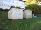 Två små ljusgula igenbommade ekonomibyggnader (kiosker) tillhörande Hällesåkers dansbana år 2010. De står på en gräsmatta. I bakgrunden ses en större byggnad.
Relaterade motiv: 2024_1119 - 1137.