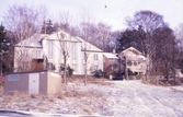 I förgrunden till vänster ses ett elskåp. Rakt fram ligger Svenska Missionskyrkan på Störtfjällsgatan 130 (tidigare: Trädgårdsgatan), 1970-tal. Till höger ses ett gult bostadshus på Störtfjällsgatan 128 (Fjärdingsmannen 1). På marken ligger ett tunt lager av snö.