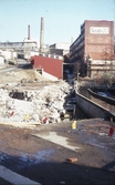 Vy från Forsebron över Kvarnfallets vattenränna samt rester efter rivningsarbeten av, troligtvis en byggnad tillhörande SOAB påKvarnbygatan 6, 1970-tal. Till vänster ses Kvarnbygatan och Soabs industriområde. Rakt fram, uppifrån, ses 