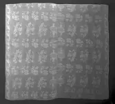 Del av duk med mönster hämtat ur Afhandling om drällers och dubbla golfmattors tillverkning, med begagnande af harnesk-rustning / författad af J.E. Ekenmark och systrar, Stockholm, 1928. Johan Erik (1786-1833), Hedda Christina ( 1786-1833), Lovisa Maria (1795-) och Gustava Fredrika, gift Beckvall (1800-).  Linnedamast, invävt DOB MLOB 1862 och märkt TA i plattsöm, från Ångermanland i privat ägo.