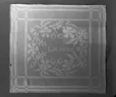 Servett med mönster hämtat ur Afhandling om drällers och dubbla golfmattors tillverkning, med begagnande af harnesk-rustning / författad af J.E. Ekenmark och systrar, Stockholm, 1928. Johan Erik (1786-1833), Hedda Christina ( 1786-1833), Lovisa Maria (1795-) och Gustava Fredrika, gift Beckvall (1800-).  Linnedamast, invävt LS 1832, vävt av Björkanders linneväveri i Visby, Gotland. I privat ägo.